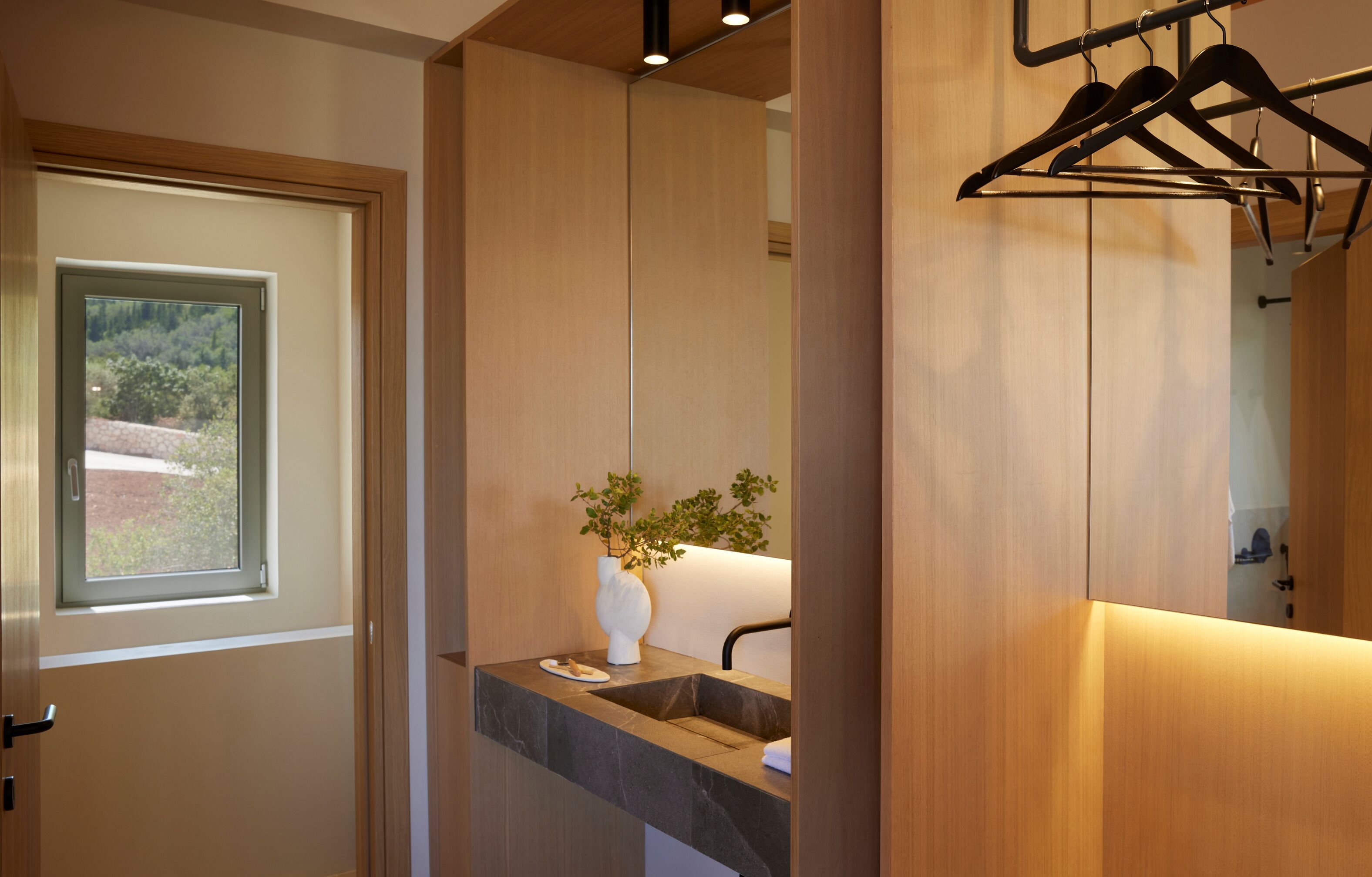 Un baño moderno con tocador de madera, ventana, planta y espejo.