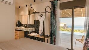 A modern hotel room with a large bed, a bathroom with a marble countertop, and a view of the sea through the sliding glass door.