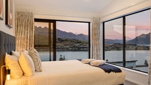A bedroom with a large bed, curtains, and a view of mountains and a lake. - St Matthews Views - Cecil (Queenstown)