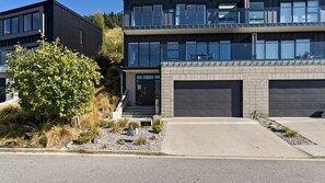 A modern two-story building with a garage, a small front yard with a tree, and a clear sky. - St Matthews Views - Cecil (Queenstown)