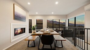 A dining area with a fireplace, a table set for four, and a scenic mountain view through large windows. - St Matthews Views - Cecil (Queenstown)