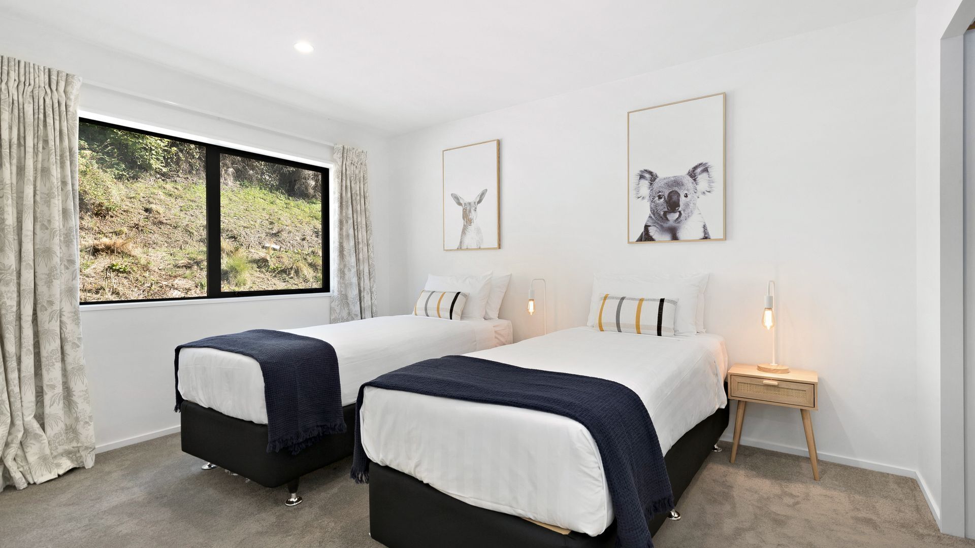 Een slaapkamer met twee bedden, een raam met uitzicht op groen en twee ingelijste foto's aan de muur.