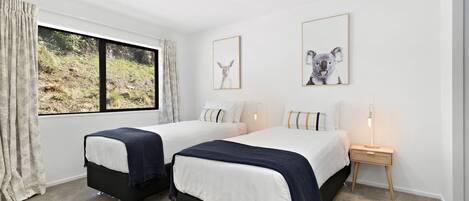 Een slaapkamer met twee bedden, een raam met uitzicht op groen en twee ingelijste foto's aan de muur.