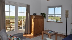 A room with a large sliding glass door leading to an outdoor area with a table and chairs, a wooden cabinet with a plant, and a small table with a magazine. - Cottage detached for ref; https://www.vrbo.com/nl-nl/vakantiewoning/p1114020 (Alphen aan den Rijn)