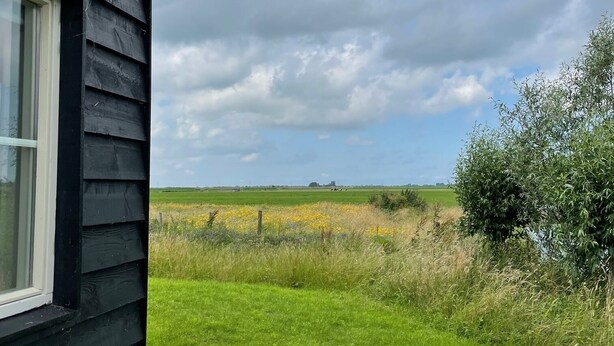 A black wooden house with a window, a grassy yard, and a field in the background. - Cottage detached for ref; https://www.vrbo.com/nl-nl/vakantiewoning/p1114020 (Alphen aan den Rijn)