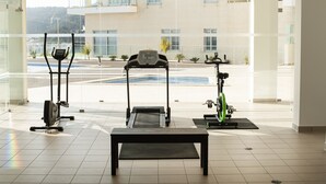 Ett gym med träningsutrustning, inklusive löpband, crosstrainer och motionscykel, med utsikt över en byggnad och träd utanför.
