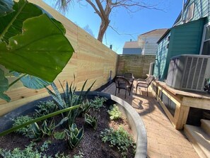 A backyard with a wooden fence, a patio with chairs, and an air conditioning unit.