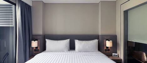 A modern hotel room with a large bed, two bedside tables with lamps, a large window with curtains, and a view of the city.