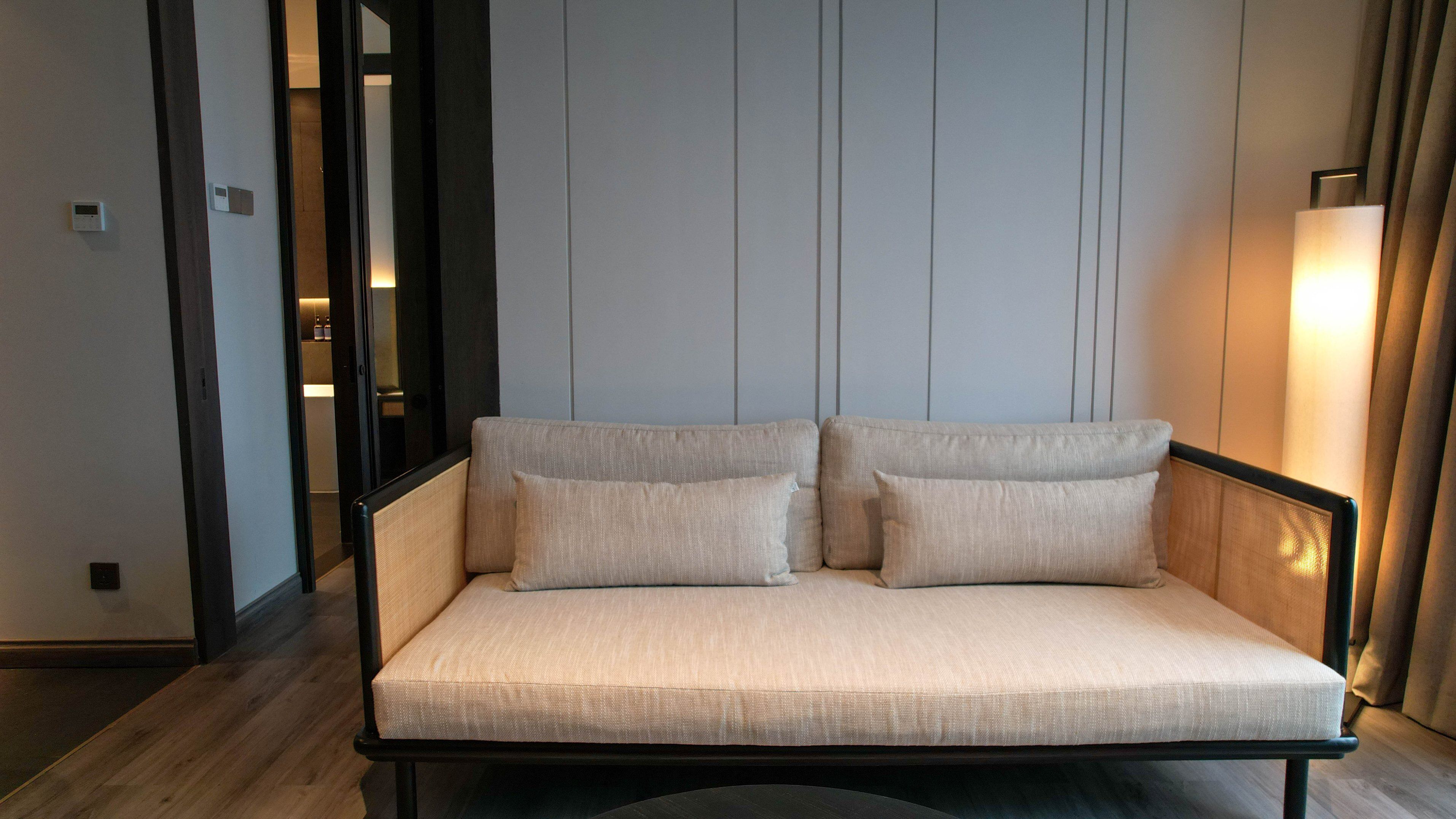 A modern sofa with two cushions in a hotel room with a wooden floor and a light-colored wall.