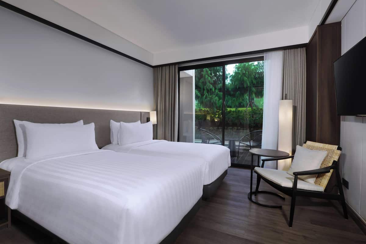 A hotel room with a large bed, a chair, a TV, and a view of greenery outside.