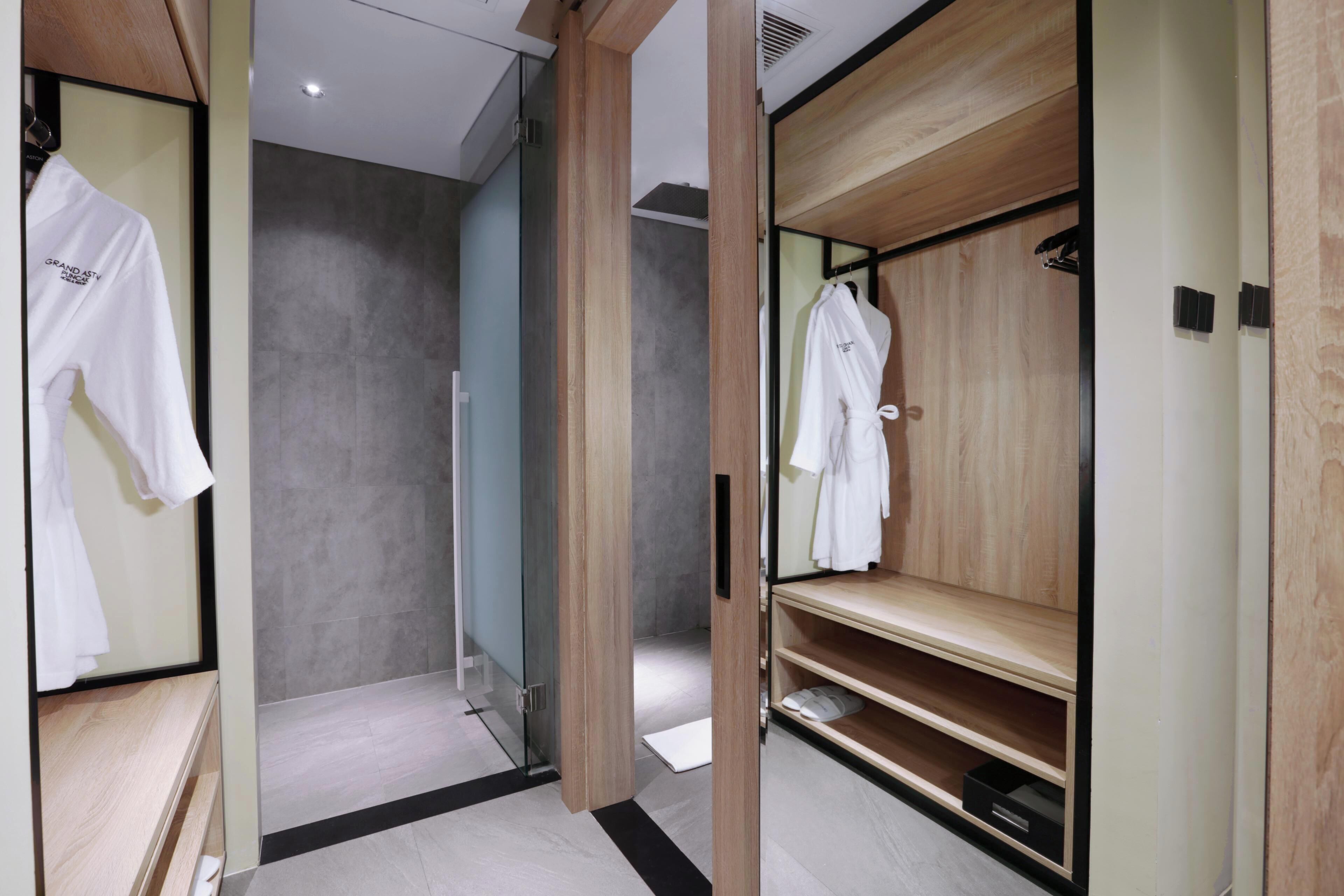 Ein modernes Badezimmer mit Duschkabine aus Glas, Holzwaschtisch und Kleiderhaken für Bademäntel.