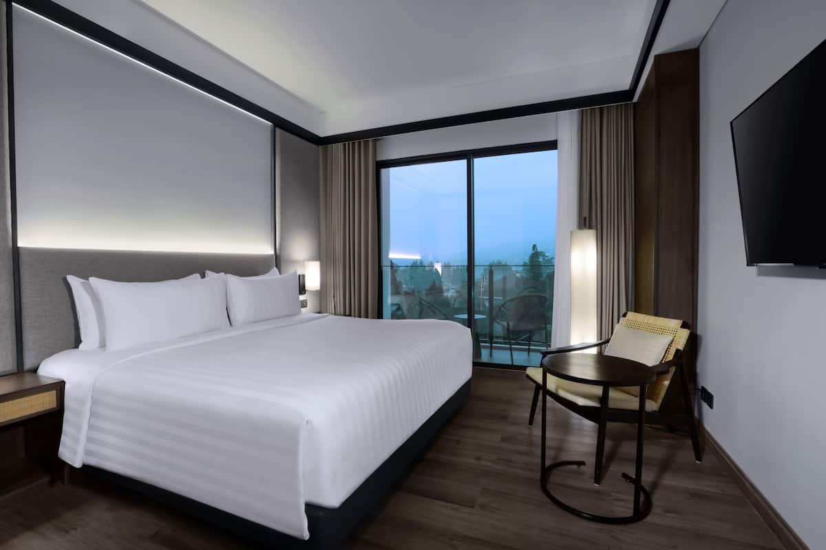 A hotel room with a large bed, a small table, a chair, a TV, and a balcony with a view.