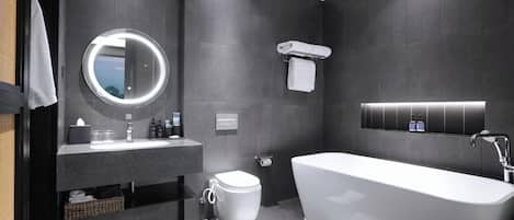 Un baño moderno con una bañera independiente, un espejo redondo con luz, un inodoro y un perchero para toallas.