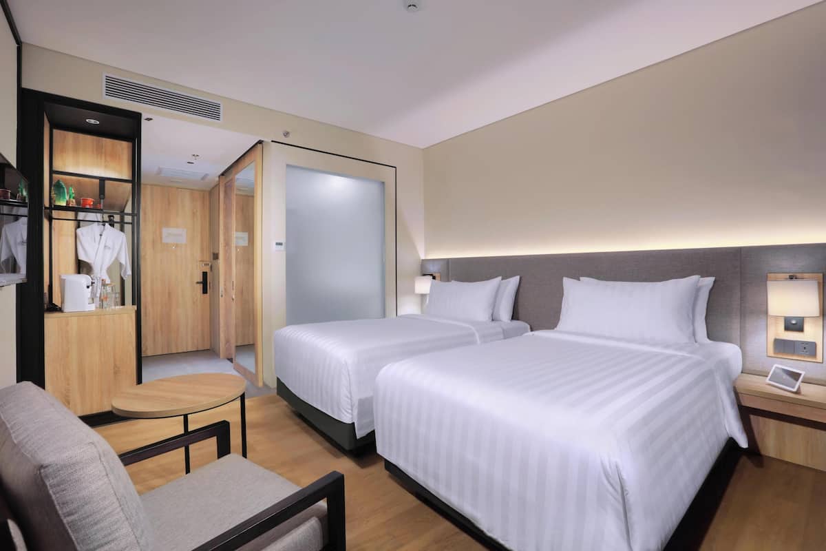 A hotel room with two beds, a small table, a chair, a desk with a lamp, and a wardrobe.