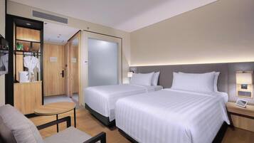 Habitación de hotel con dos camas, una mesita, una silla, un escritorio con lámpara y un armario.