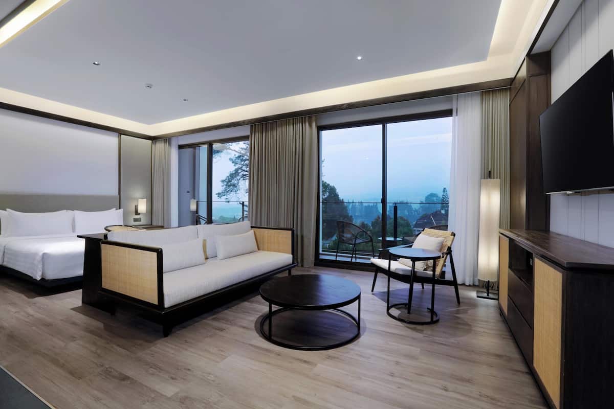 A modern hotel room with a large bed, a sofa, a dining table, and a TV.