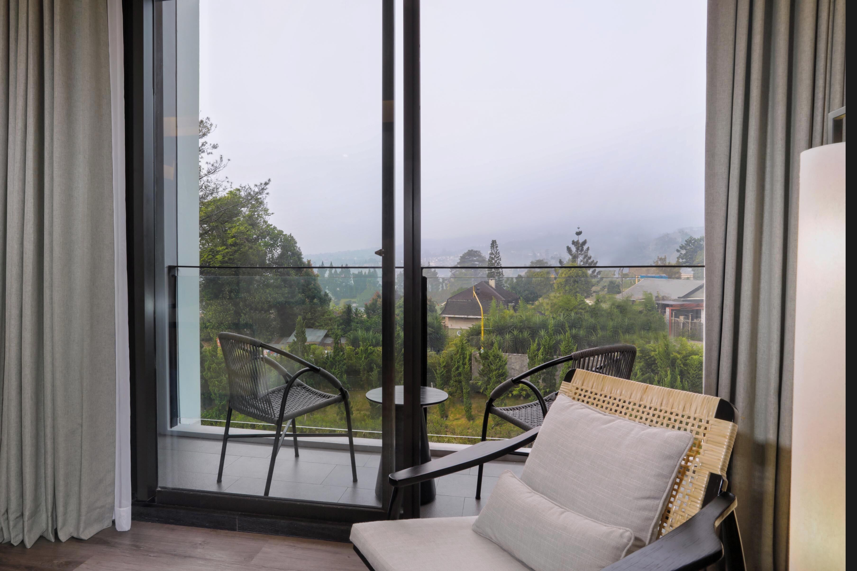 A balcony with a view of greenery and buildings, a wicker chair, and a small table.