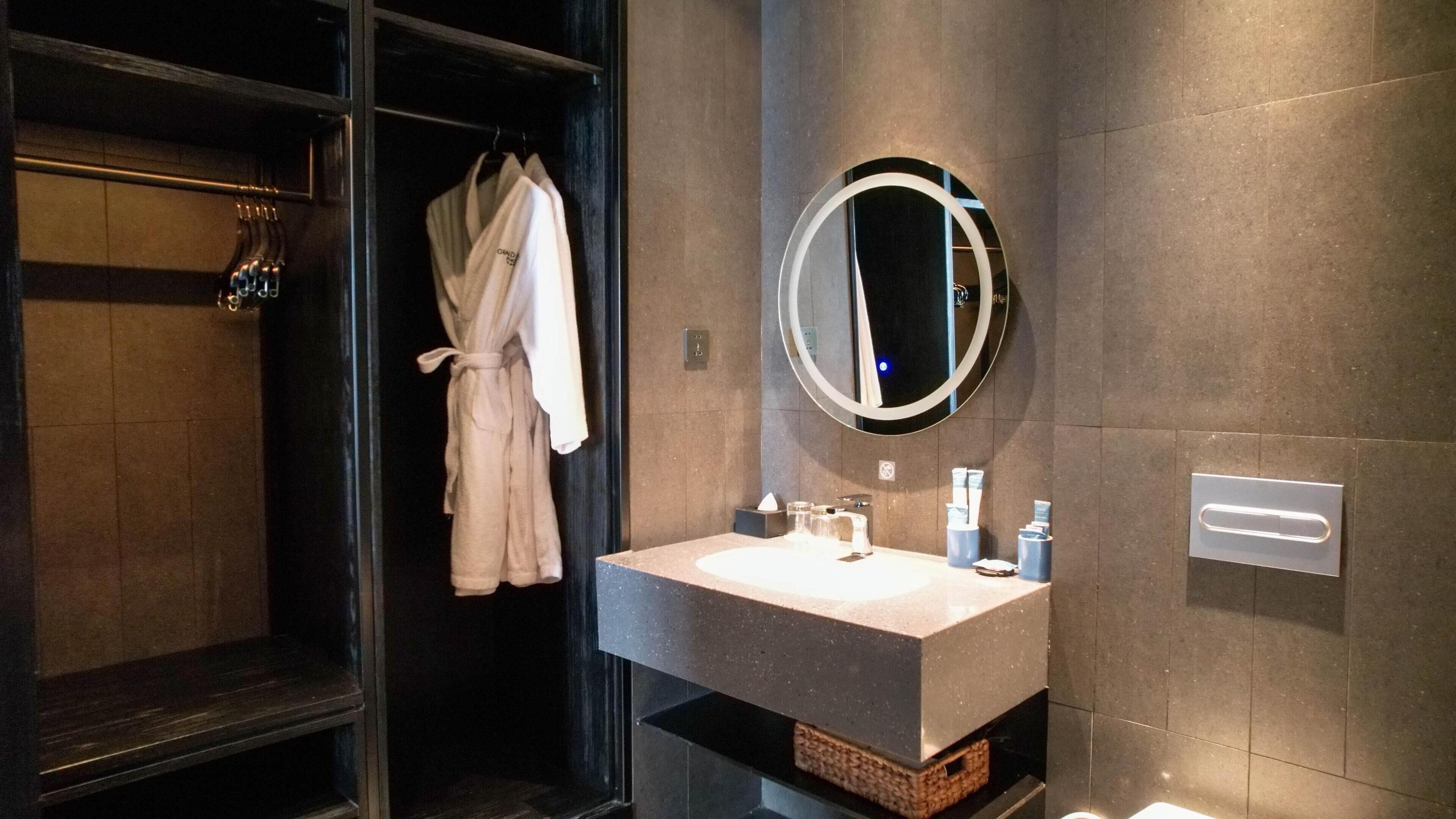 A modern bathroom with a dark wood vanity, a round mirror, and a robe hanging on a rack.