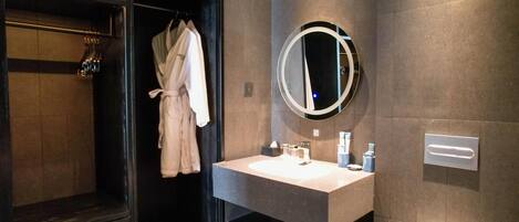 A modern bathroom with a dark wood vanity, a round mirror, and a robe hanging on a rack.
