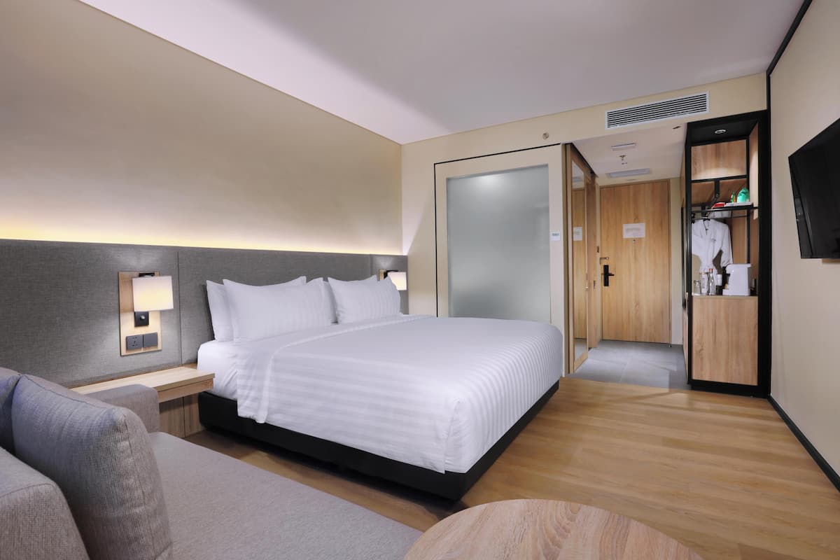 A modern hotel room with a large bed, bedside tables, a sofa, a TV, and a walk-in closet.
