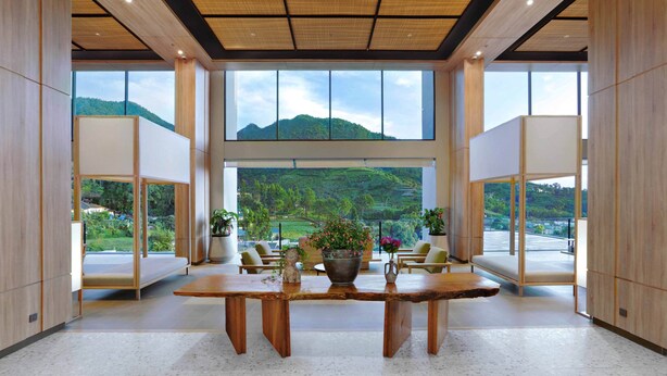 Una habitación amplia con una gran mesa de madera, zona de estar y ventanas grandes que ofrecen vistas a un paisaje verde.