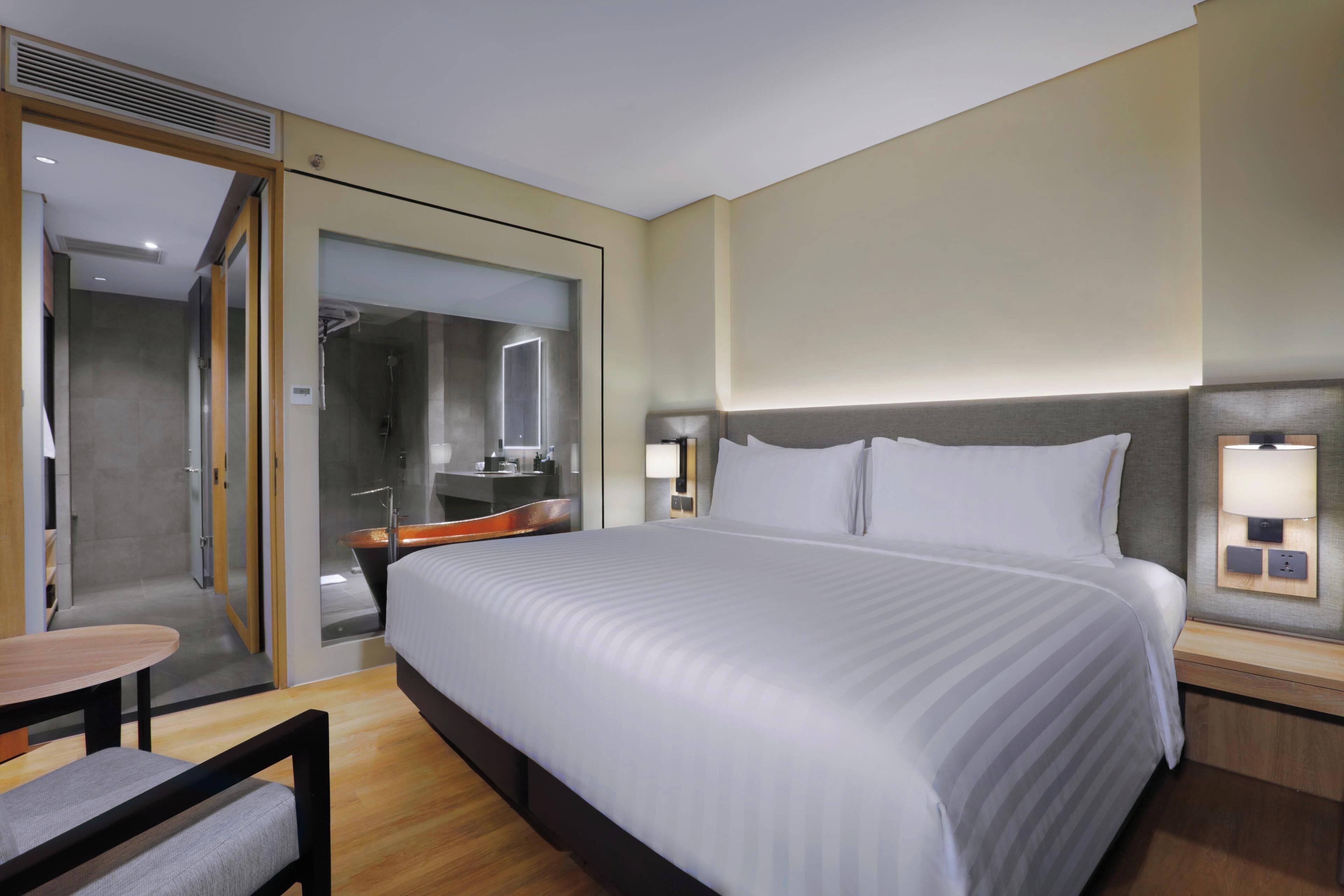 A modern hotel room with a large bed, a desk, and a shower area.