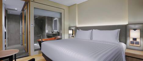 A modern hotel room with a large bed, a desk, and a shower area.
