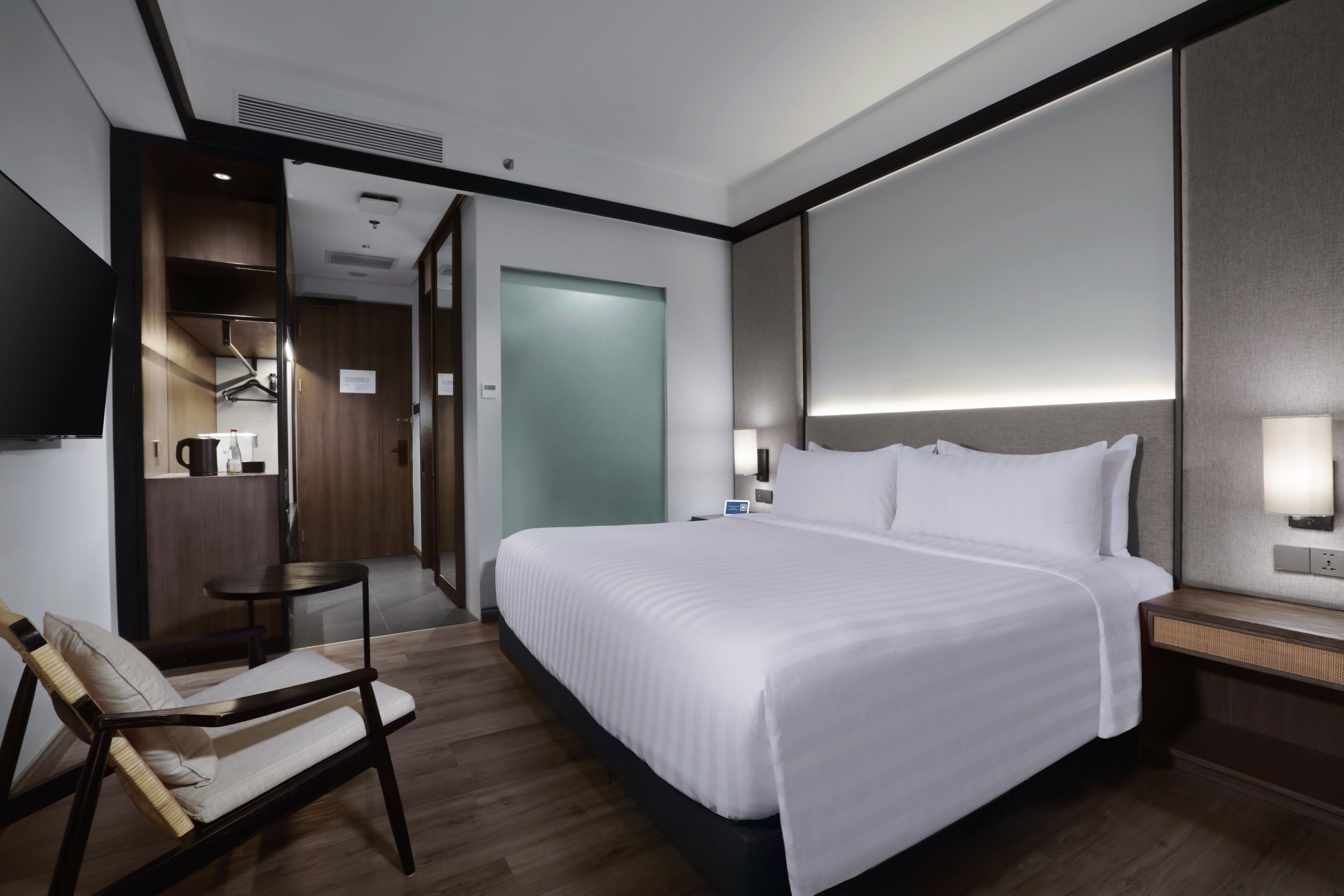 Una habitación de hotel moderna con una cama grande, una mesita de noche, una silla y una pequeña mesa.