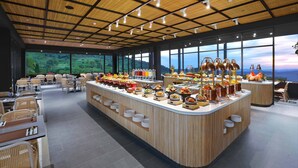 Un área de bufé con diversas opciones de comida, un espacio de asientos con mesas y sillas, y grandes ventanales con vistas al exterior.