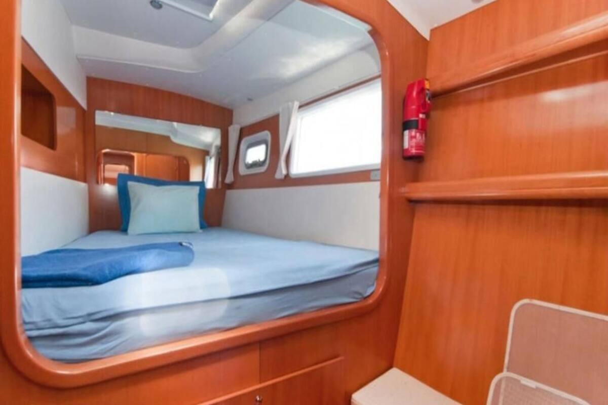 A compact cabin with a single bed, a small window, and a fire extinguisher mounted on the wall.