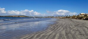 Una spiaggia con una battigia sabbiosa, cielo sereno e edifici in lontananza.