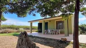 Un edificio con un patio cubierto, una mesa con sillas y un pequeño jardín.