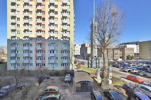 A multi-story residential building with balconies, a parking area with cars, and a clear sky.