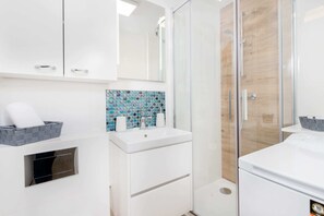 A modern bathroom with a white sink, a mirror, a shower, and a tiled backsplash.