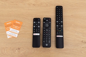 Three remote controls and two orange cards on a wooden surface.