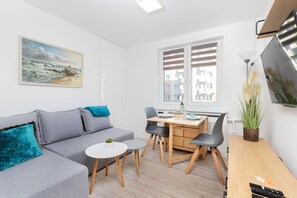 A modern living room with a sofa, a dining table, chairs, a small round table, and a TV.