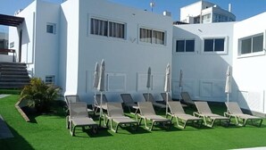 Un bâtiment blanc doté d’un espace piscine comprenant des chaises longues et des parasols.