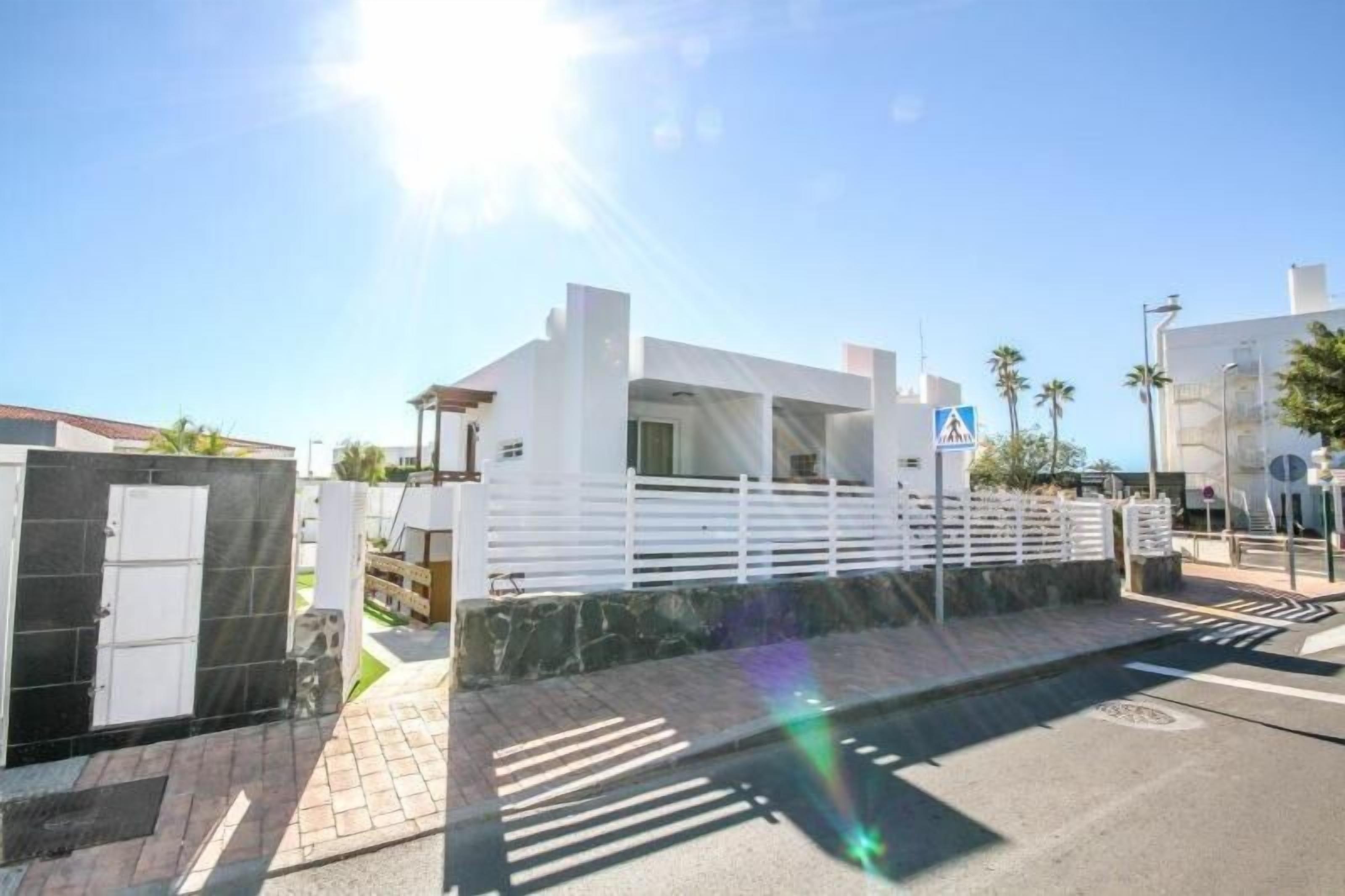 A modern building with a white facade, a gated entrance, and a paved driveway.