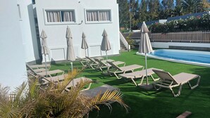 Un espace piscine agrémenté de gazon synthétique, de chaises longues et de parasols.