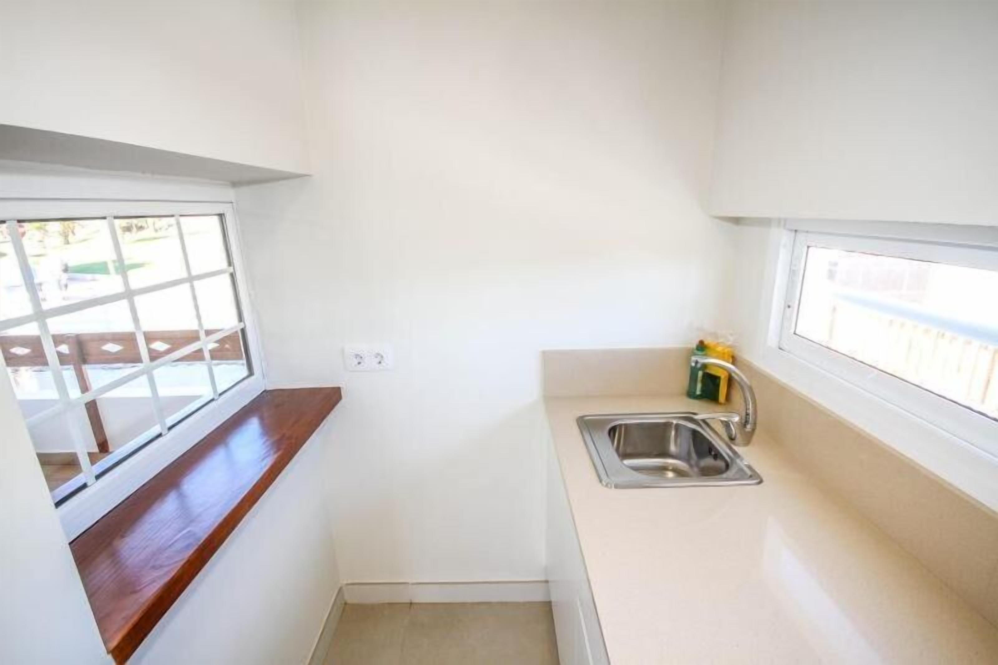 Una pequeña cocina con ventana, un lavamanos y un estante de madera.