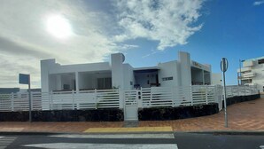 Un bâtiment moderne à la façade blanche, doté d’une entrée sécurisée par un portail et d’une zone pavée devant.