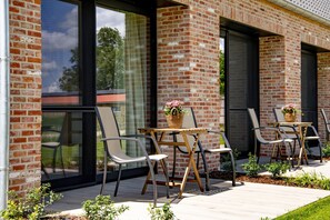 A patio with outdoor seating, a brick wall, and a glass door. - B&B 't Motjeshof (Pittem)