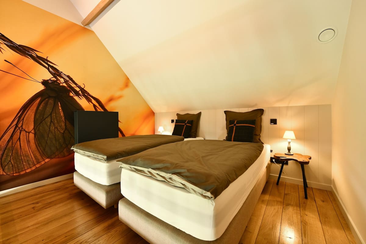 A cozy loft bedroom with a sloped ceiling, a large bed, a small bedside table with a lamp, and a wall mural.