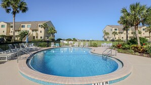 Ein Pool mit einer Tiefe von 1,80 Metern, umgeben von Liegestühlen und Palmen, mit Apartmentgebäuden im Hintergrund.