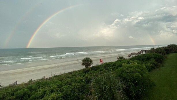 Ein Strand mit Regenbogen, Wellen und einer Holzpromenade.