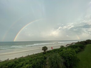 Een strand met een regenboog, golven en een houten looppad.