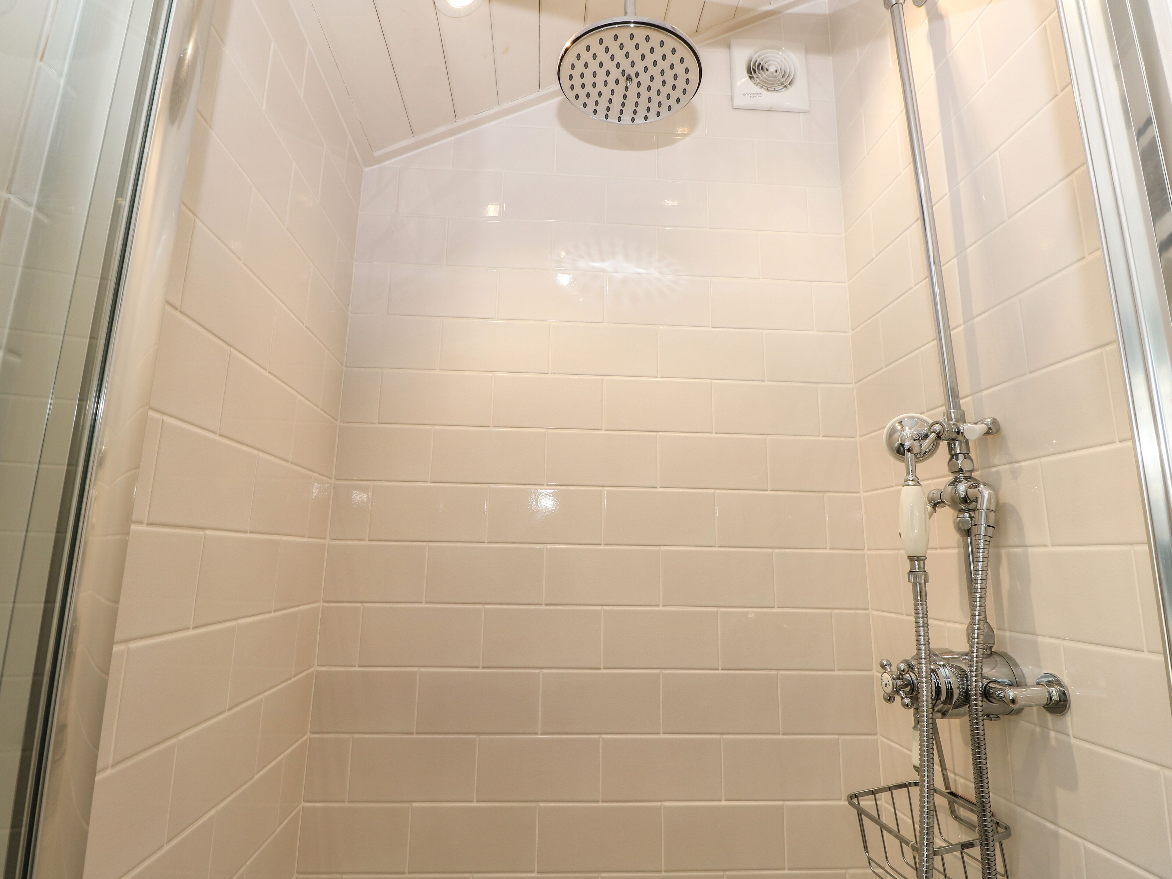 A shower with a handheld showerhead, a wall-mounted control panel, and a glass-enclosed shower area.