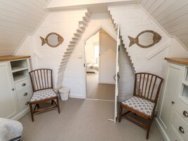 A children's playroom with two wooden chairs, a white chest of drawers, and a staircase leading to another room.