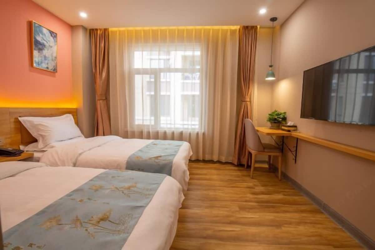 Quarto de hotel com duas camas, uma escrivaninha, uma cadeira, uma televisão e uma janela com cortinas.