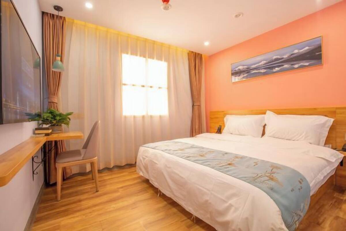 Quarto com cama, escrivaninha, cadeira, janela com cortinas e quadro na parede.